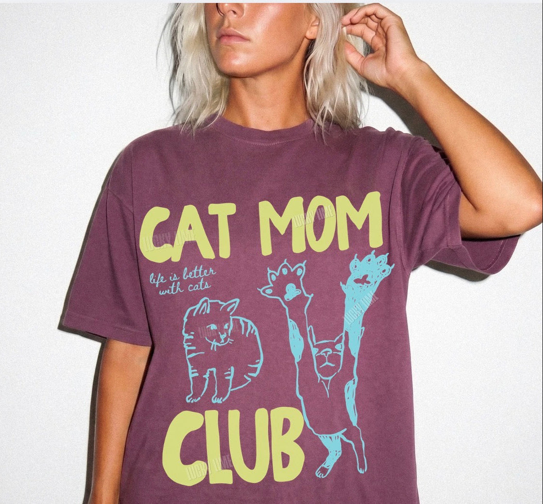 Person wearing a purple t-shirt with 'Cat Mom Club' text and cat illustrations on a white background.