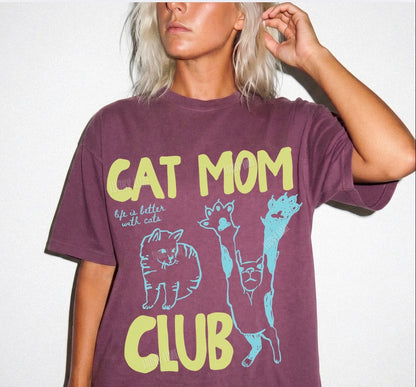 Person wearing a purple t-shirt with 'Cat Mom Club' text and cat illustrations on a white background.