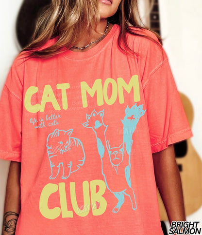 Person wearing a coral t-shirt with 'Cat Mom Club' text and graphics.