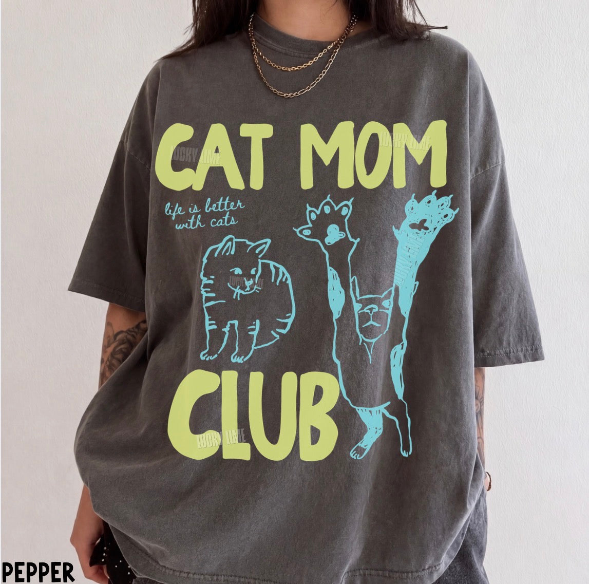 Person wearing a t-shirt with 'Cat Mom Club' text and cat illustrations.