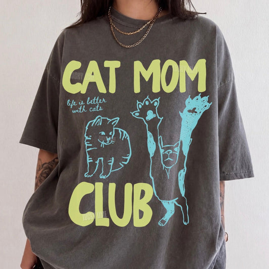 Person wearing a t-shirt with 'Cat Mom Club' text and cat illustrations.