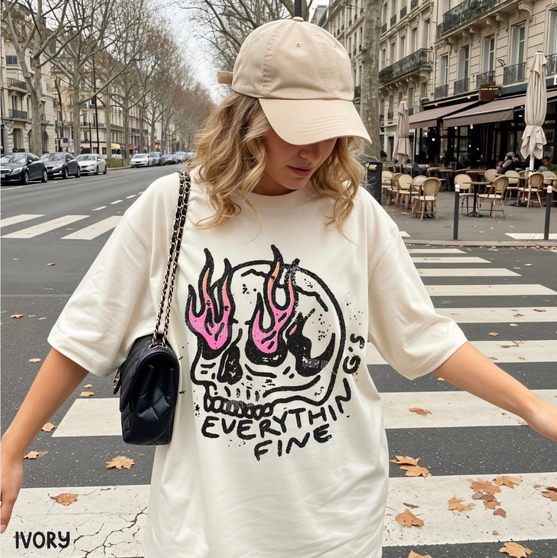Person wearing a white t-shirt with a skull design and text, standing on a city street.