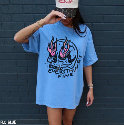 Person wearing a blue t-shirt with a skull design and 'Everything is Fine' text against a dark brick wall.