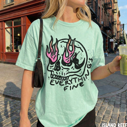 Person wearing a light green t-shirt with a skull design and text, holding a drink on a city street.