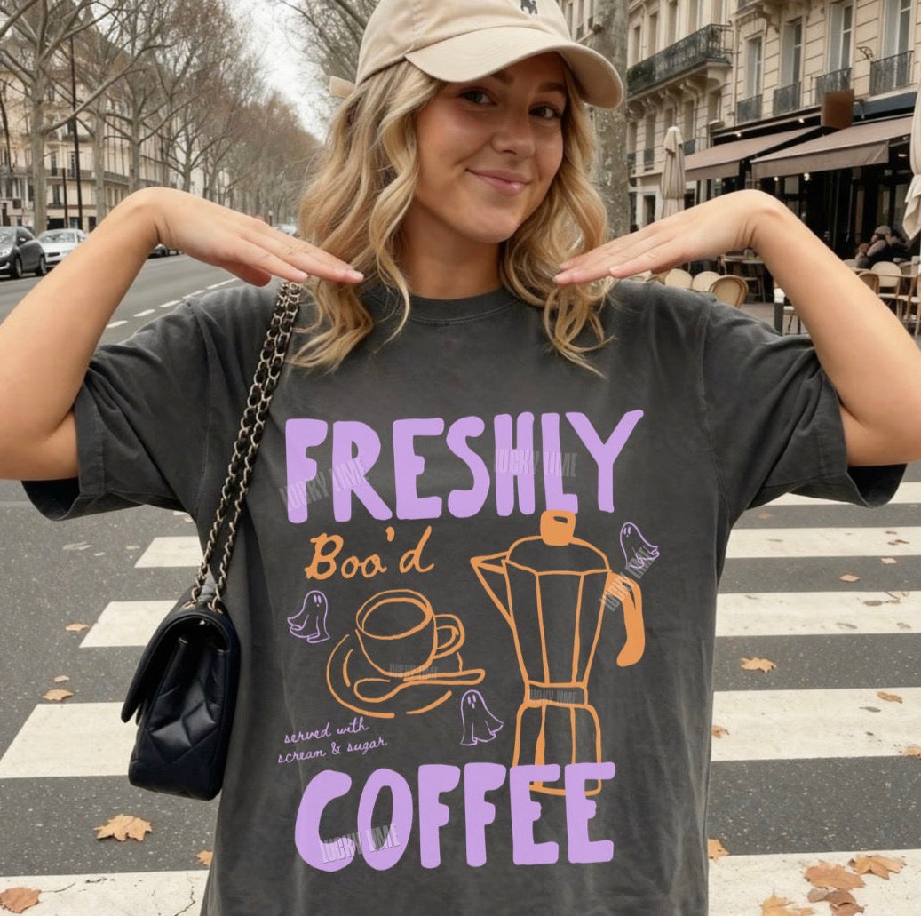 Woman wearing a t-shirt with 'Freshly Boo'd Coffee' design on a city street.