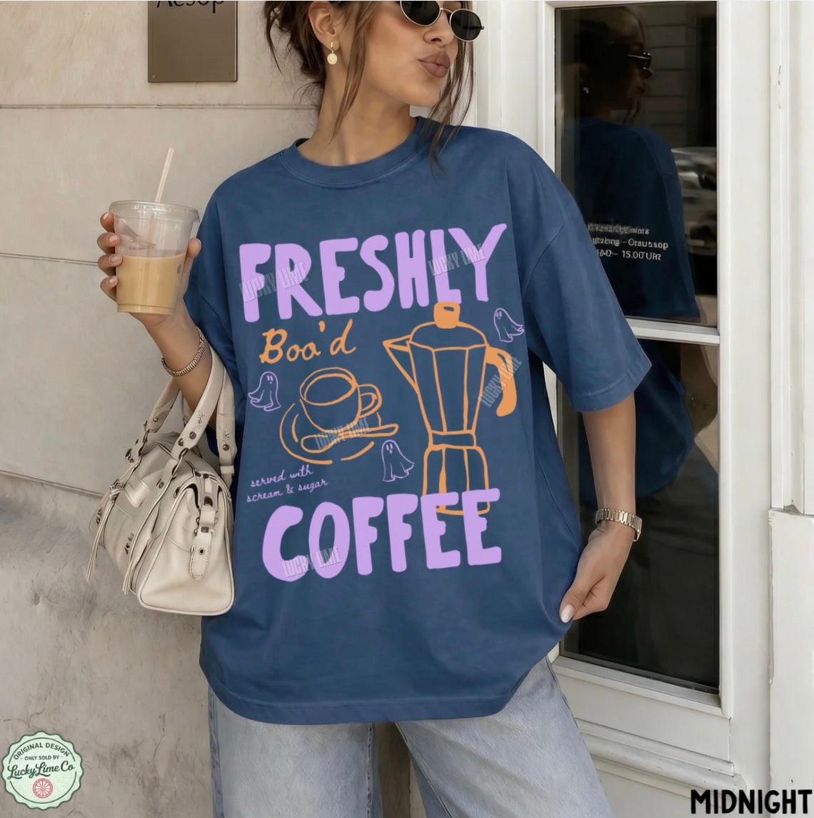 Person wearing a blue t-shirt with 'Freshly Boo'd Coffee' text and graphics, holding a drink.