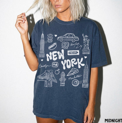 A woman wearing a dark navy blue oversized t-shirt with a white hand-drawn 'New York' graphic and city landmarks, set against a plain white background.