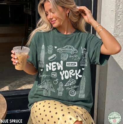 A woman wearing a dark green graphic t-shirt with white 'New York' city illustrations, holding an iced coffee in front of a storefront.