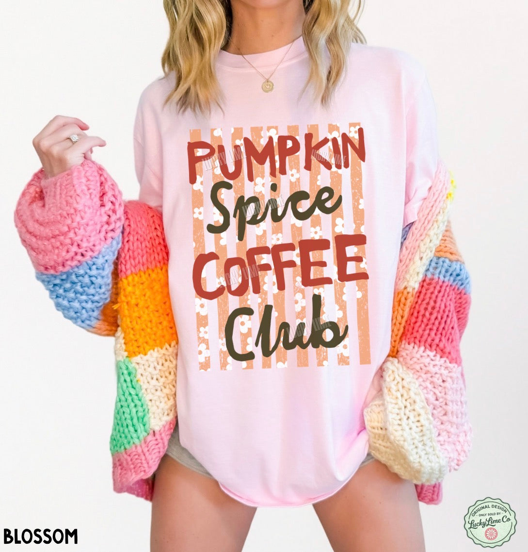 A woman wearing a light pink graphic t-shirt that reads 'Pumpkin Spice Coffee Club' in brown and black lettering, styled with a chunky rainbow knit cardigan. The brand logo 'BLOSSOM' is visible in the bottom-left corner.