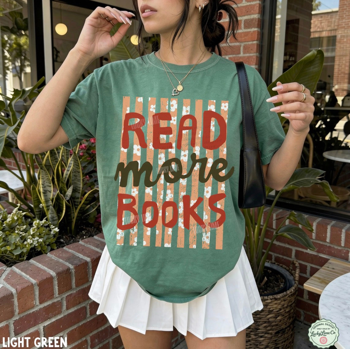 A woman wearing a light green graphic t-shirt with the text 'READ MORE BOOKS' in red and brown over a striped background, paired with a white pleated skirt and a black shoulder bag.