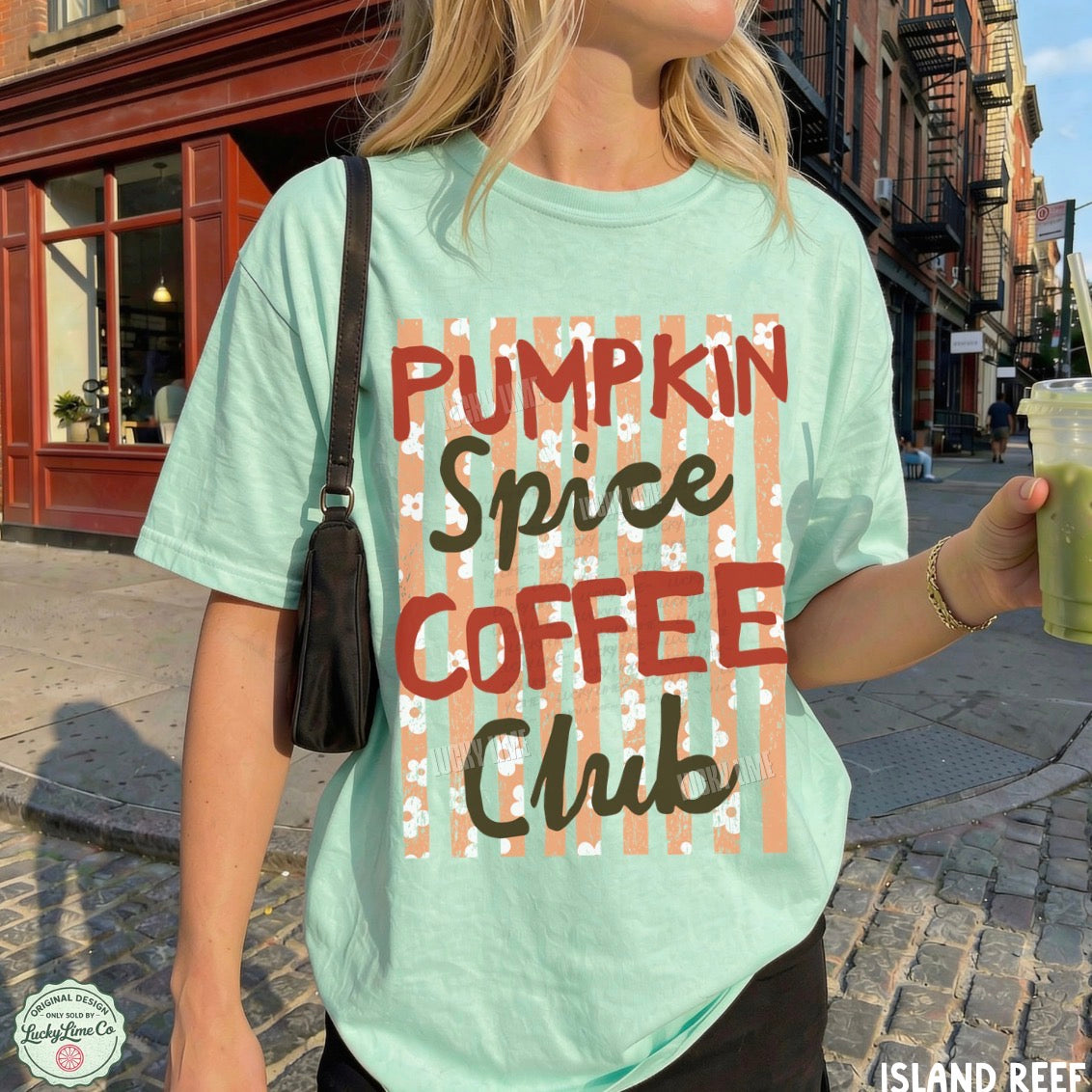 A woman wearing a mint green graphic t-shirt with 'PUMPKIN SPICE COFFEE CLUB' printed on the front, standing on a cobblestone street.