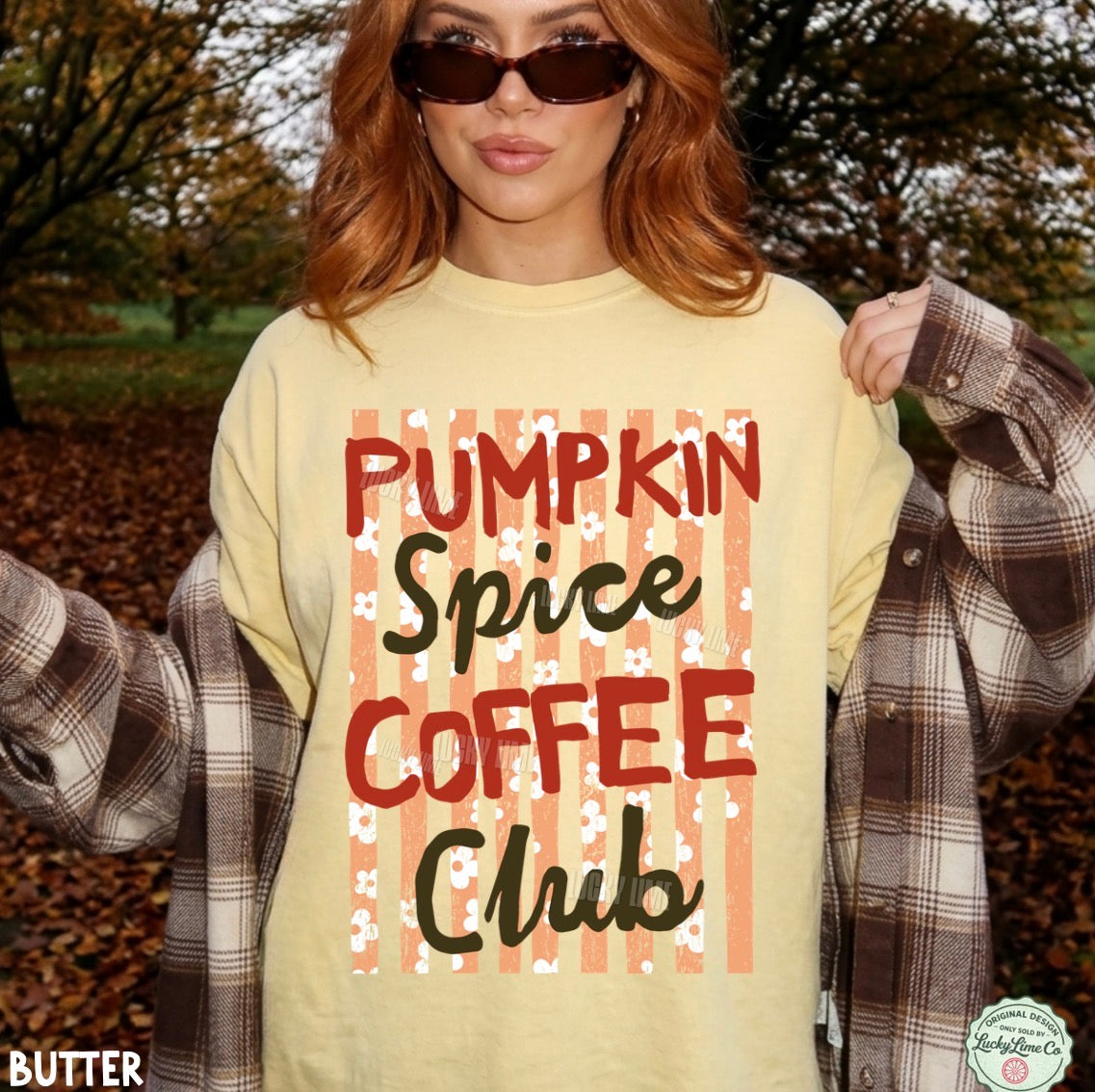 A woman outdoors wearing a pale yellow graphic T-shirt that reads 'Pumpkin Spice Coffee Club' over peach vertical stripes, with a brown-and-white plaid flannel shirt draped off her shoulders. She is also wearing dark sunglasses.