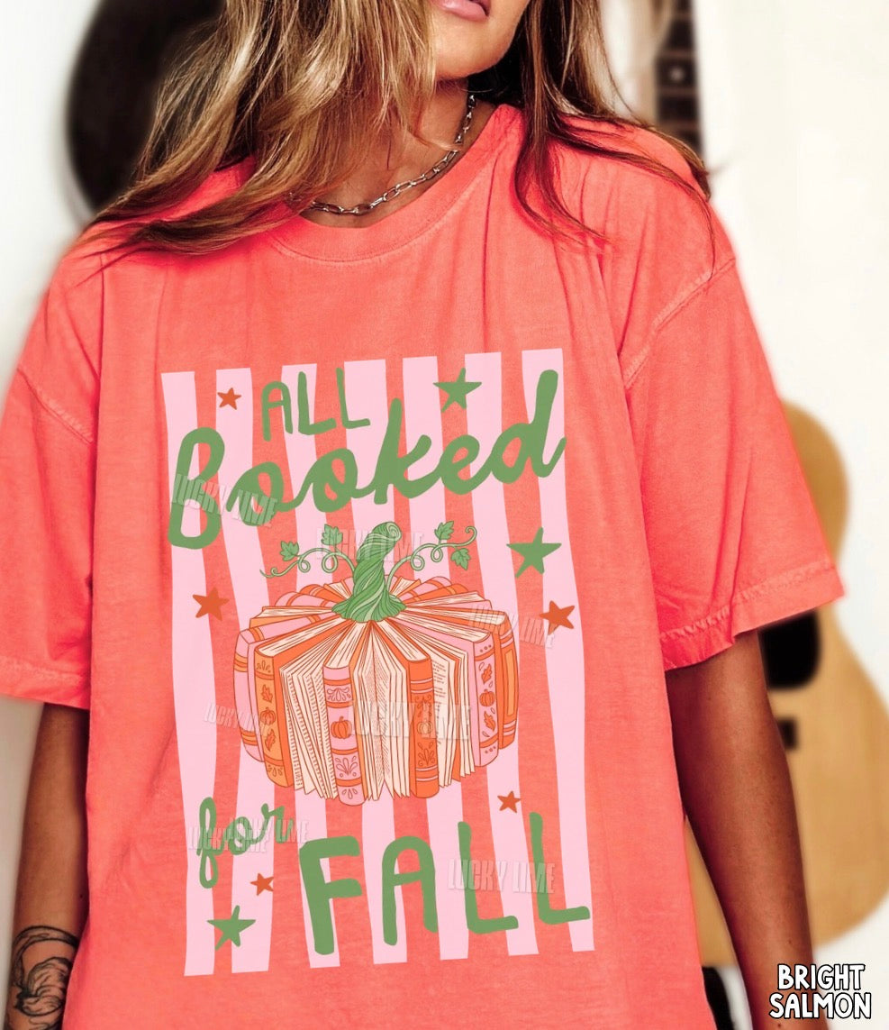 A woman wearing a coral pink graphic t-shirt with a green and white design that reads 'ALL Booked for FALL' with a book bundle illustration. The t-shirt has a visible watermark 'BRIGHT SALMON' on the bottom right corner.