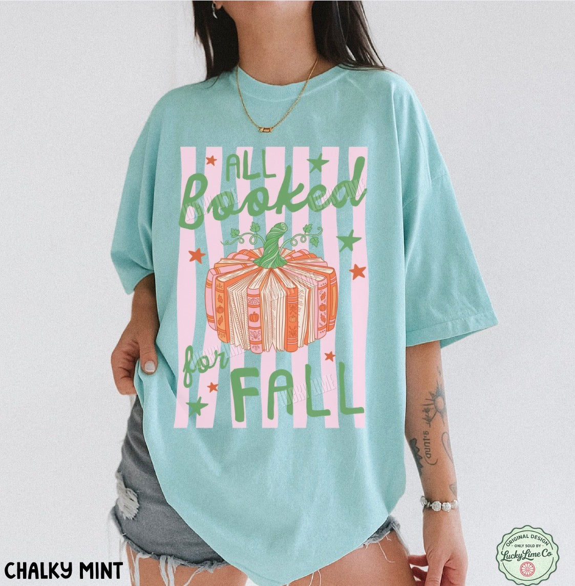 A woman wearing an oversized light mint green graphic t-shirt with a fall-themed design featuring a book and the words 'ALL Booked for FALL'.