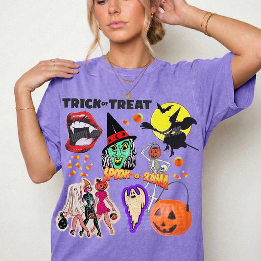 A woman wearing a lavender purple t-shirt with a colorful Halloween graphic print featuring 'Trick or Treat' text, a witch, a jack-o'-lantern, and other spooky characters, set against a plain light background.