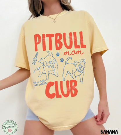 A woman wearing a pale yellow graphic T-shirt with red and blue text reading 'PITBULL mom CLUB' and dog illustrations, shown against a plain light background.