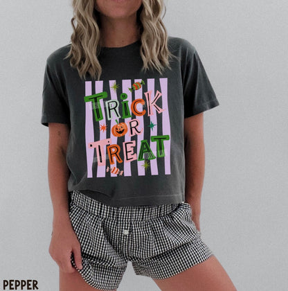 A woman wearing a dark charcoal gray graphic t-shirt with a 'Trick or Treat' Halloween design and black-and-white gingham shorts, standing against a light gray background.