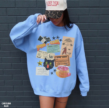 A person wearing an oversized light blue sweatshirt with a collage-style graphic print on the front, paired with a white cap, standing against a dark gray brick wall. The sweatshirt graphic includes vintage-style ticket, newspaper, star, cat, and donut illustrations.