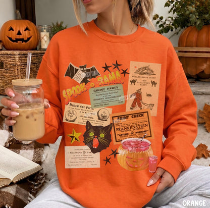 A woman wearing an orange crewneck sweatshirt with a vintage-style Halloween collage print, holding an iced coffee in a glass jar in a cozy, autumn-themed setting with pumpkins and fall leaves.
