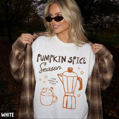 A woman outdoors wearing a white graphic T-shirt with 'Pumpkin Spice Season' text and pumpkin spice latte illustrations, styled with a brown plaid shirt draped off her shoulders and dark sunglasses.