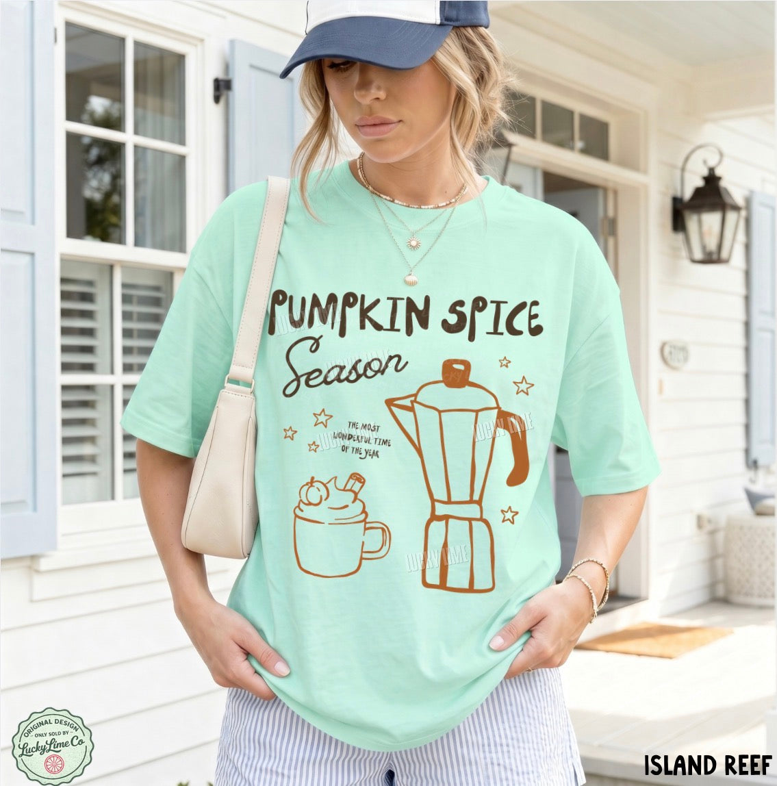 A woman wearing a mint green graphic t-shirt with 'Pumpkin Spice Season' text and illustrations of a coffee mug and moka pot, posed on a porch. The brand 'Island Reef' is visible in the bottom right corner.