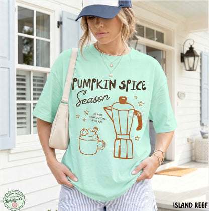 A woman wearing a mint green graphic t-shirt with 'Pumpkin Spice Season' text and illustrations of a coffee mug and moka pot, posed on a porch. The brand 'Island Reef' is visible in the bottom right corner.