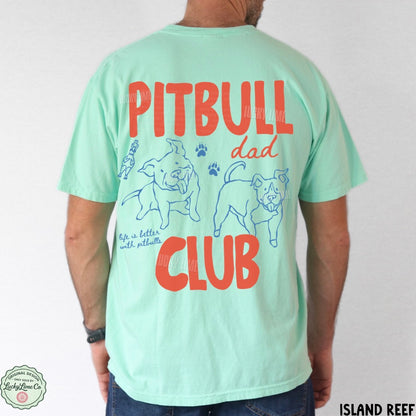 A man wearing a mint green t-shirt from the back, featuring a graphic print with the words 'PITBULL dad CLUB' in red and blue illustrations of pitbull dogs. The brand 'Island Reef' is visible on the bottom right corner and as a watermark/logo on the shirt.