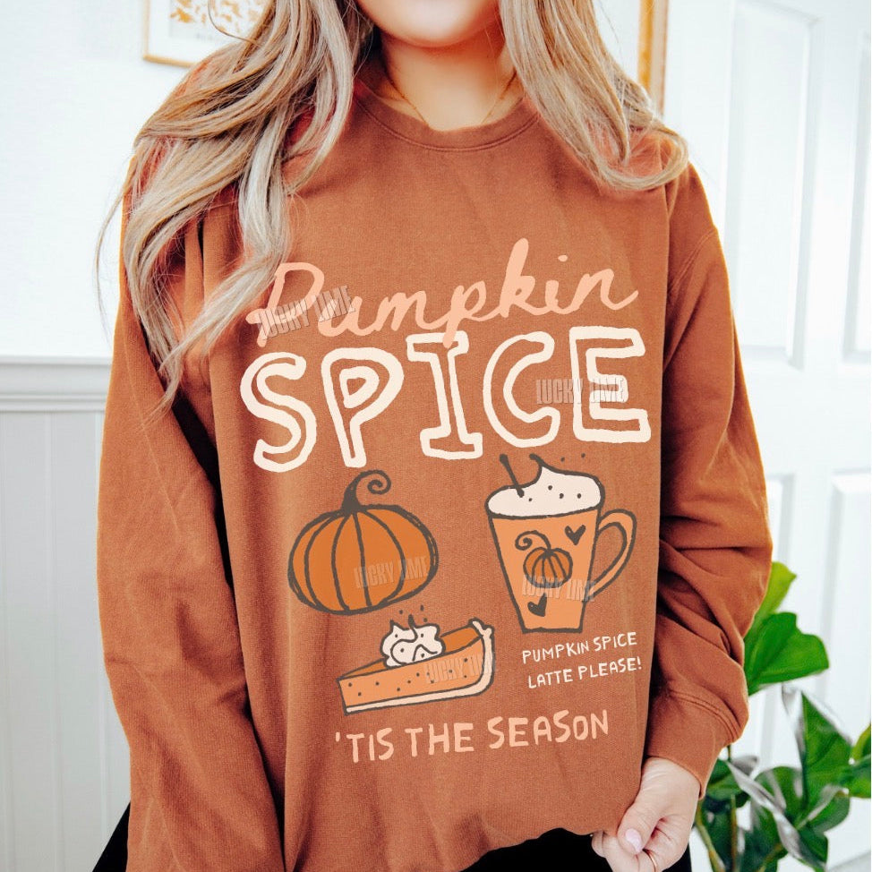 A woman wearing a brown crewneck sweatshirt with a 'Pumpkin Spice' graphic print featuring a pumpkin, latte, and pie, with the text 'Pumpkin Spice Latte Please! Tis the Season'.