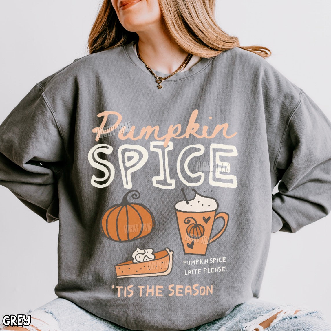 A woman wearing a gray oversized sweatshirt with a 'Pumpkin Spice' autumn graphic featuring a pumpkin, latte, and pie. The sweatshirt has a white and peach text design with a small 'GREY' label in the bottom-left corner.