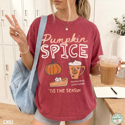 A woman wearing a faded red graphic t-shirt with 'Pumpkin Spice' text and autumn illustrations, holding an iced coffee and wearing a denim shoulder bag in a bright indoor setting.