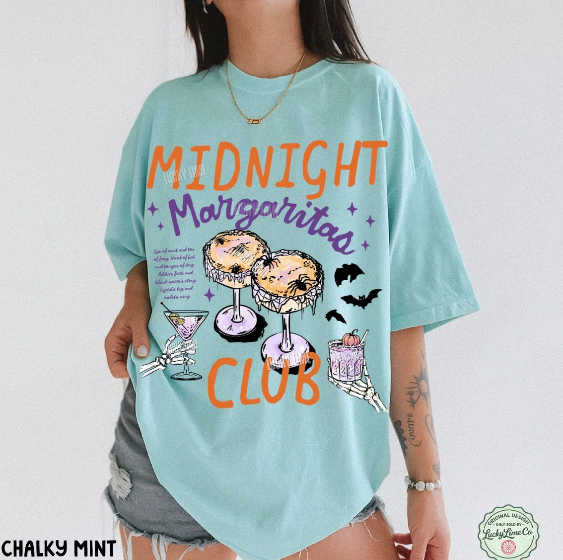 A woman wearing an oversized light aqua graphic t-shirt with 'MIDNIGHT Margaritas CLUB' printed in orange and purple, featuring illustrations of margaritas and bats. The image has a white background with a watermark logo in the bottom right corner.