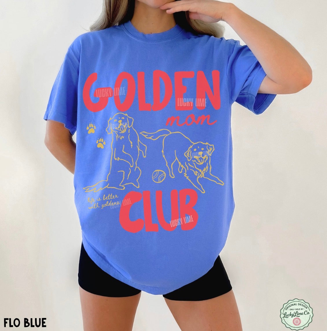 A woman wearing a bright blue graphic t-shirt with red and yellow text and dog illustrations, paired with black shorts, against a plain light background.