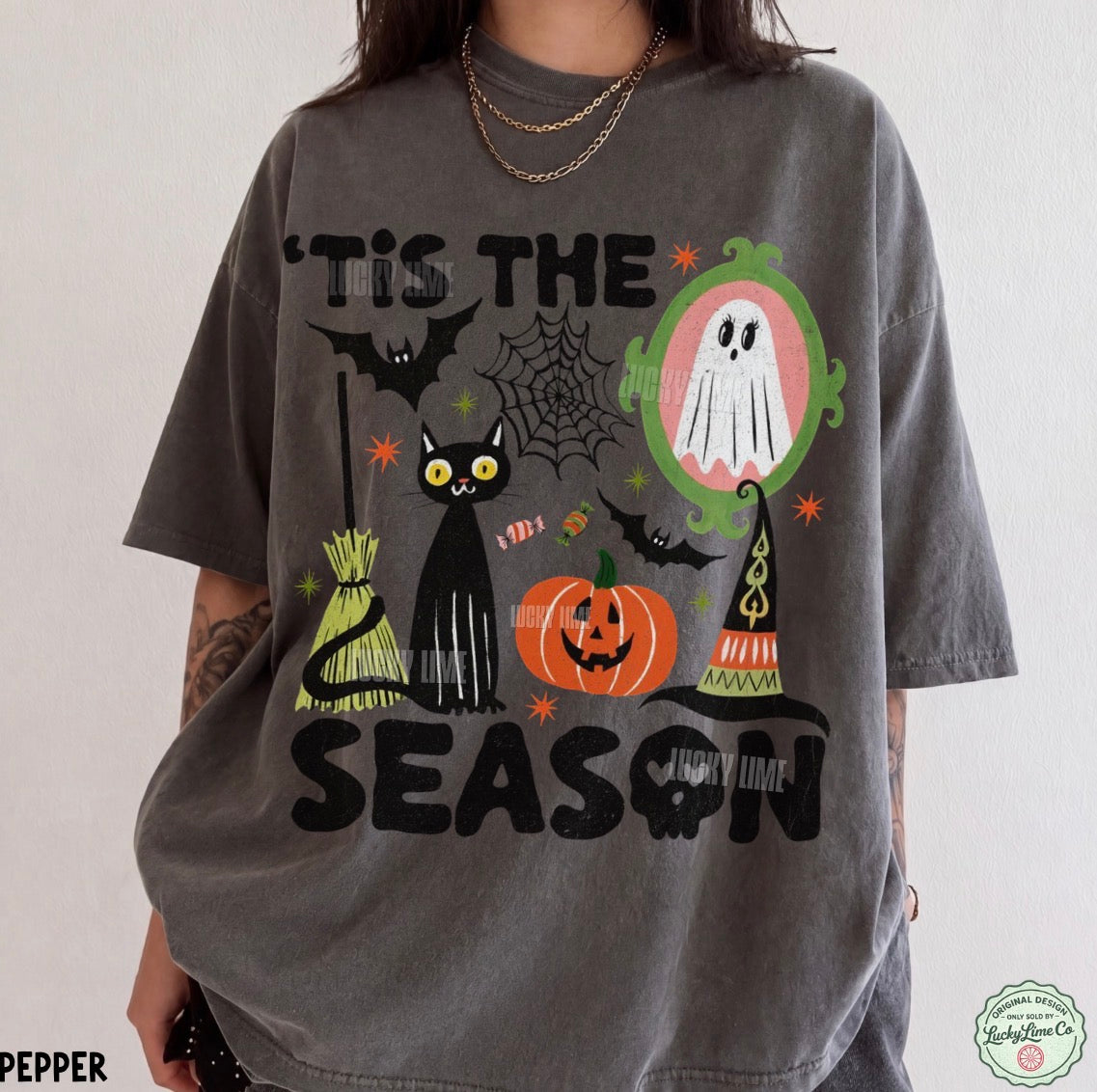 A person wearing an oversized charcoal gray graphic T-shirt with Halloween-themed illustrations including a black cat, jack-o'-lantern, ghost, bats, spiderwebs, and the text “IT’S THE SEASON” and “Happy Time.”.