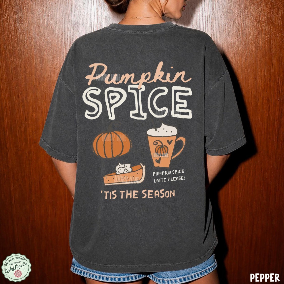 A person shown from the back wearing an oversized dark charcoal T-shirt with a large autumn-themed graphic that reads “Pumpkin Spice” and includes a pumpkin, slice of pie, mug, and “Tis the season” text. The photo is taken against a wooden door background.