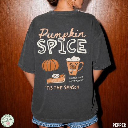 A person shown from the back wearing an oversized dark charcoal T-shirt with a large autumn-themed graphic that reads “Pumpkin Spice” and includes a pumpkin, slice of pie, mug, and “Tis the season” text. The photo is taken against a wooden door background.
