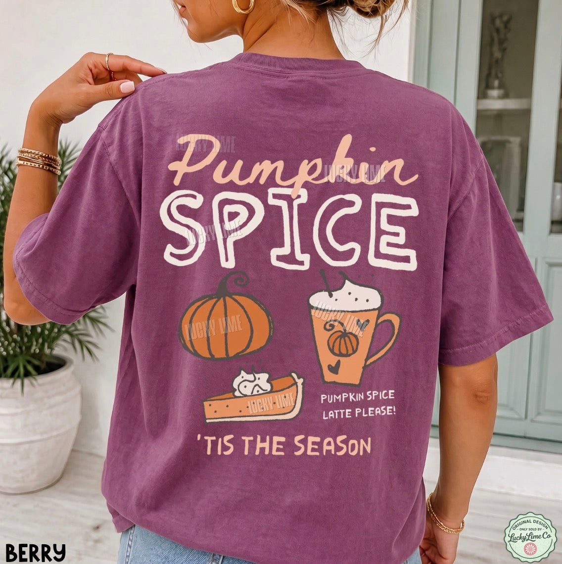 A woman shown from the back wearing a purple short-sleeve graphic T-shirt with 'Pumpkin Spice' and fall-themed illustrations on the back, photographed in a bright indoor setting.