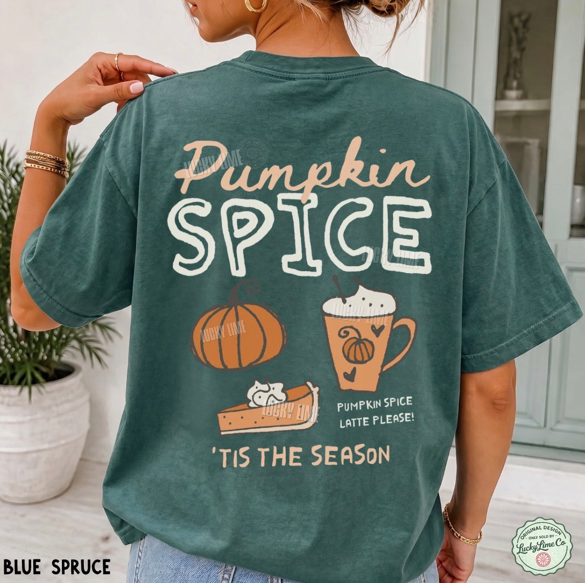 A woman wearing a faded teal-blue short-sleeve graphic T-shirt, shown from the back in a bright indoor setting. The shirt features the words 'Pumpkin Spice' in peach and white lettering, with illustrations of a pumpkin, a slice of pie, a mug with whipped cream, and the phrase 'Tis the Season'.