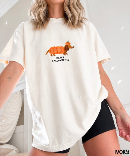 A woman wearing an oversized ivory graphic t-shirt with a cartoon dachshund dressed in a pumpkin costume and the text 'HAPPY HALLOWEENIE'.
