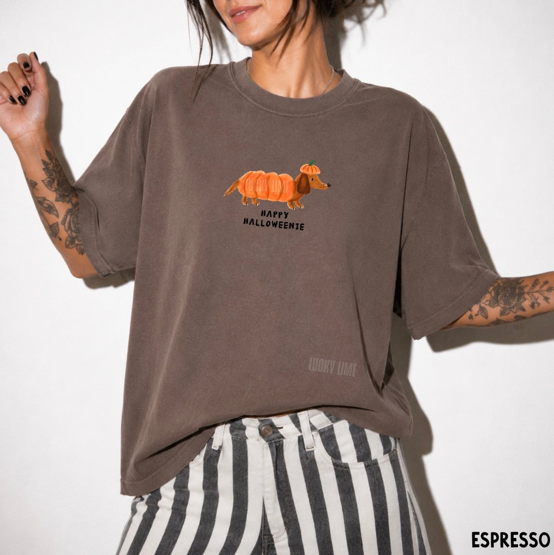 A person wearing an oversized espresso brown graphic t-shirt with a cartoon dachshund wearing a pumpkin costume and the text 'HAPPY HALLOWEENIE'.