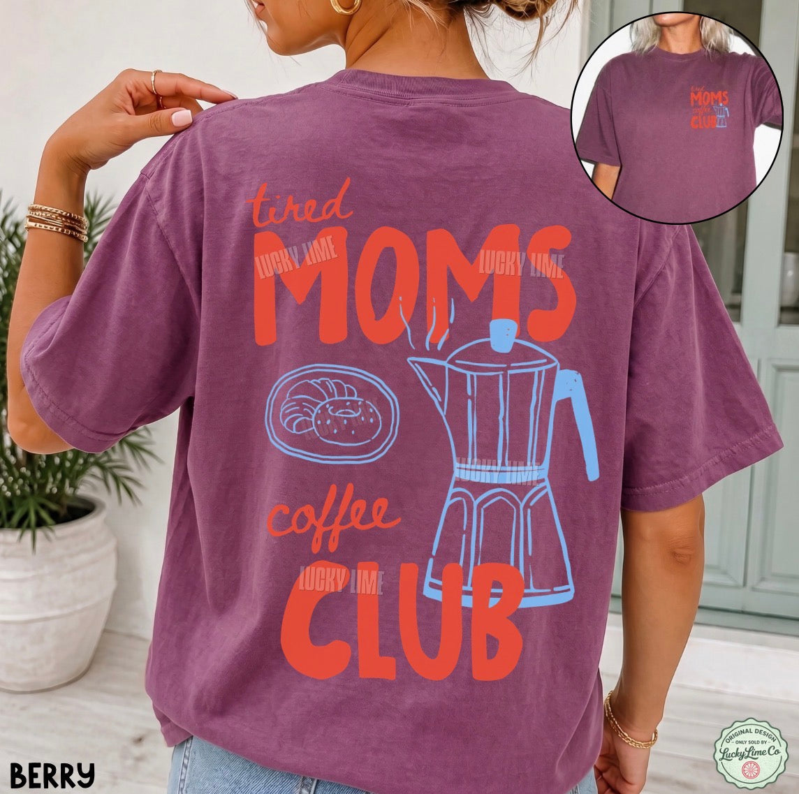 A woman wearing a berry purple t-shirt with a back graphic that reads 'Tired Moms Coffee Club' in orange and light blue, featuring a coffee pot illustration. An inset circle in the top right shows the front of the t-shirt with a matching graphic.