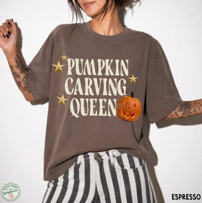 A woman wearing a brown graphic t-shirt with 'PUMPKIN CARVING QUEEN' in cream text and a jack-o'-lantern graphic, paired with black and white striped pants against a white background.