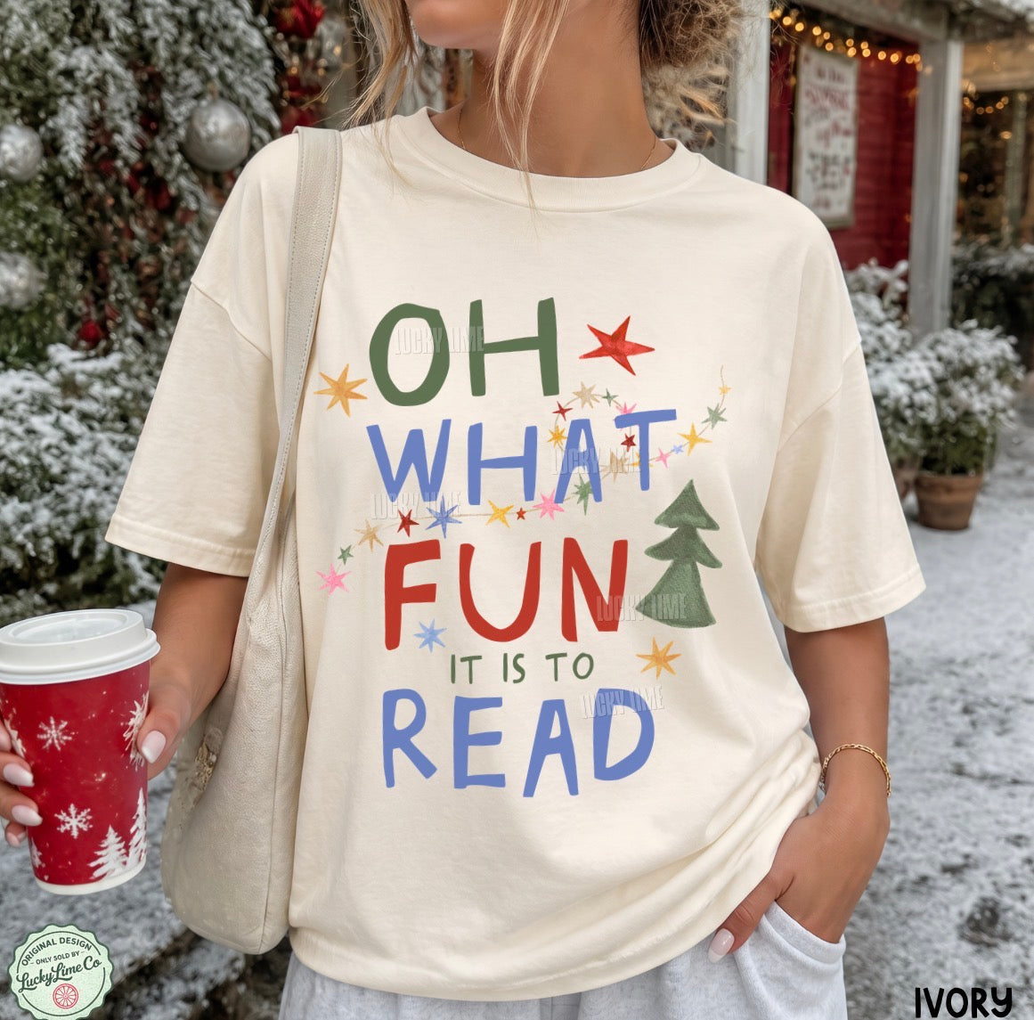 A woman wearing an ivory graphic t-shirt with the text 'OH WHAT FUN IT IS TO READ' in colorful hand-drawn letters, holding a red Starbucks coffee cup in a snowy outdoor setting.