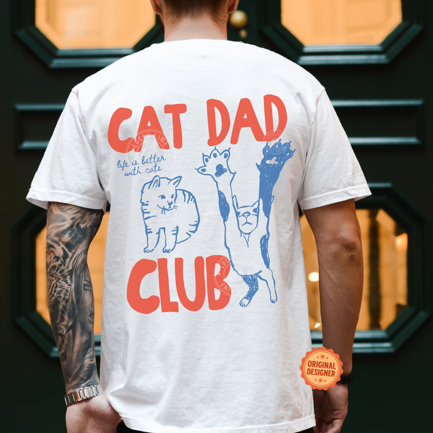 Person wearing a white t-shirt with 'Cat Dad Club' design and tattoos on arm.