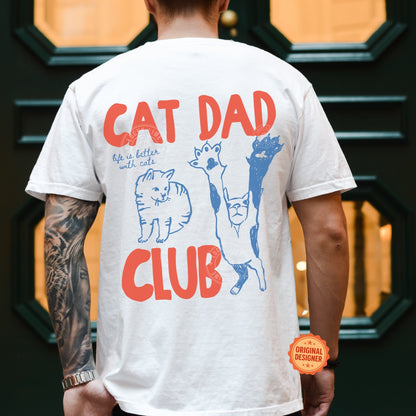 Person wearing a white t-shirt with 'Cat Dad Club' design and tattoos on arm.