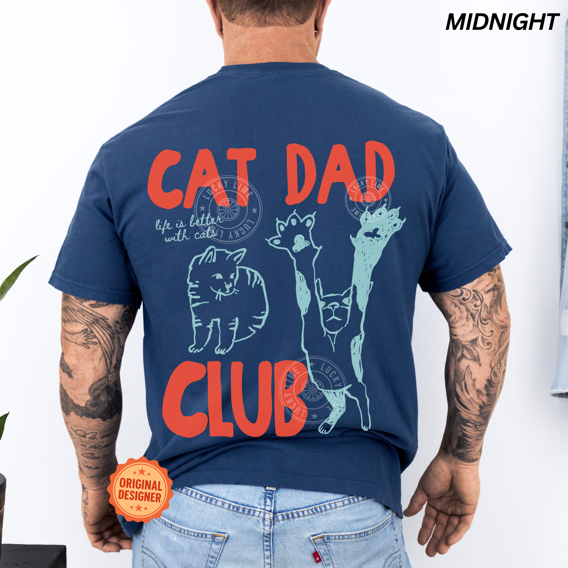 Person wearing a navy blue t-shirt with 'Cat Dad Club' design on the back, with tattoos visible.