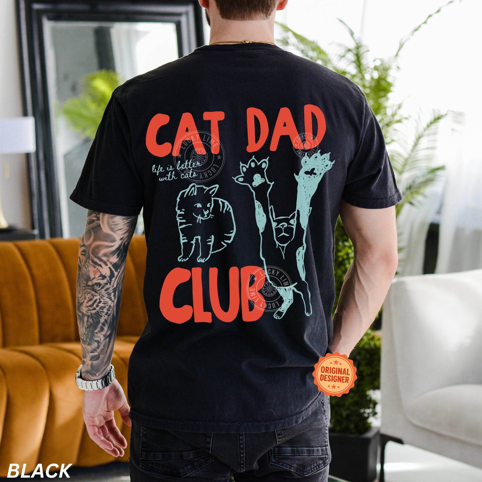 Person wearing a black t-shirt with 'Cat Dad Club' design in a living room.