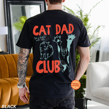 Person wearing a black t-shirt with 'Cat Dad Club' design in a living room.