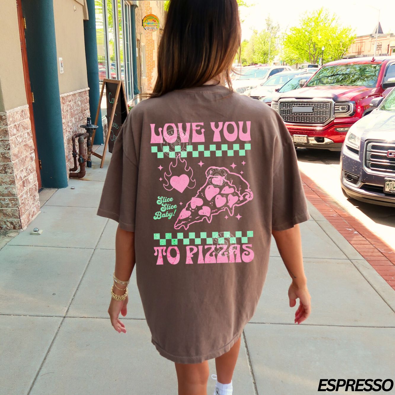 Person wearing a brown t-shirt with a pizza-themed design on the back, standing on a sidewalk.
