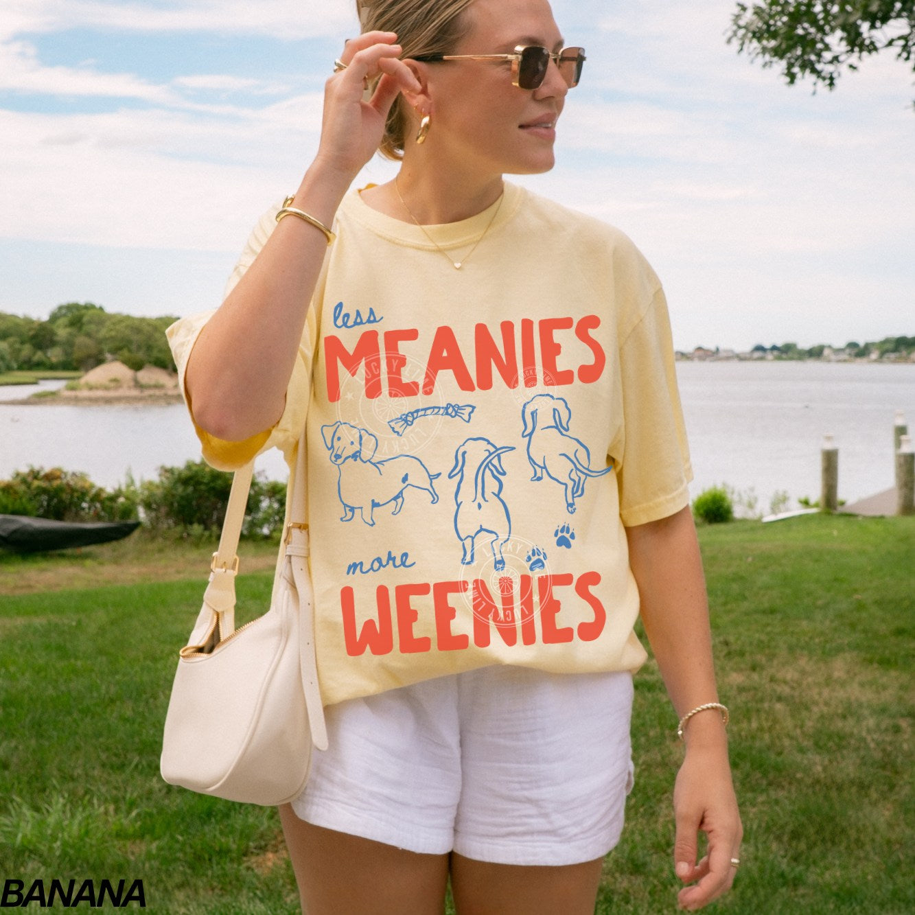 Woman wearing a yellow t-shirt with dachshund design that says ‘less meanies more weenies’ by a lake