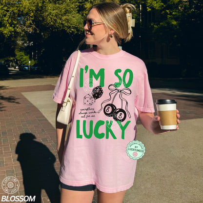 Person wearing a pink t-shirt with 'I'm so lucky' text and graphics, holding a coffee cup on a sidewalk.